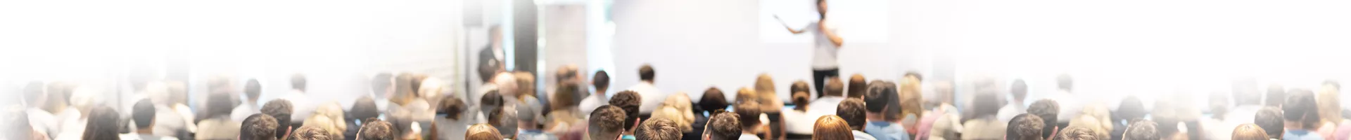 A speaker presenting in front of the audience with focus on the audience.