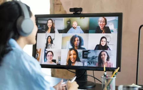 Image of woman wearing headphones smiling and listening to a group of people through a computer screen.