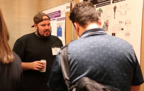 A man stands in front of his scientific poster to discuss with another man who has his back to the camera.